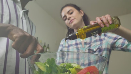 Woman pouring olive oil over salad