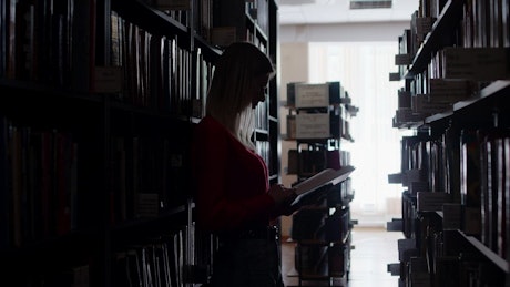 Woman reading a book in a dark library.