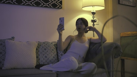 Woman resting on a sofa while talking on video call.