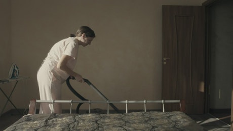 Woman running a vacuum cleaner over the carpet in the bedroom.