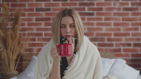 Woman shivering with a fever holding a hot beverage.