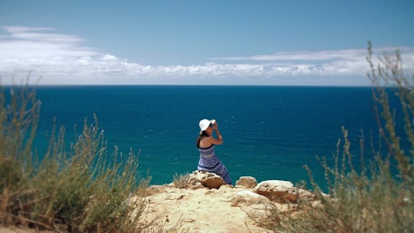 Woman sitting on the edge of a cape overlooking the sea