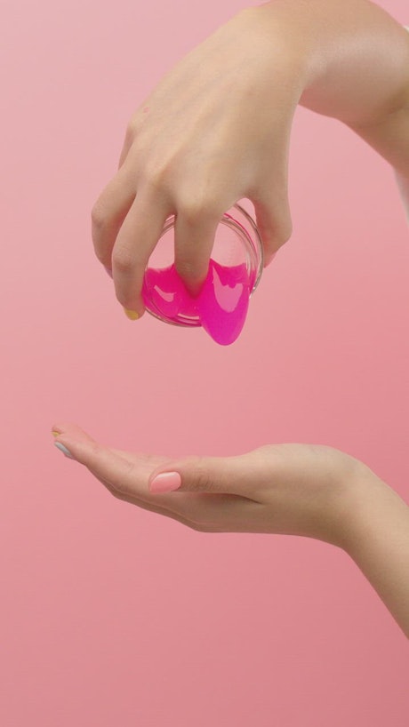 Woman spilling pink slime on her hand.