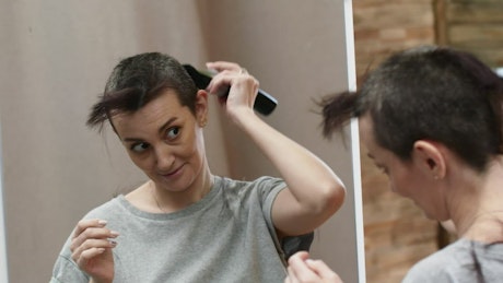 Woman standing in front of the mirror as she shaves all her hair off.