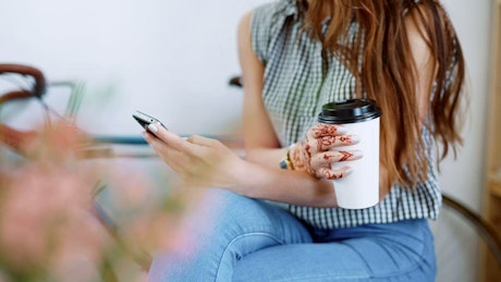 Woman texting and holding a coffee