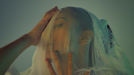 Woman touching her face above a light veil