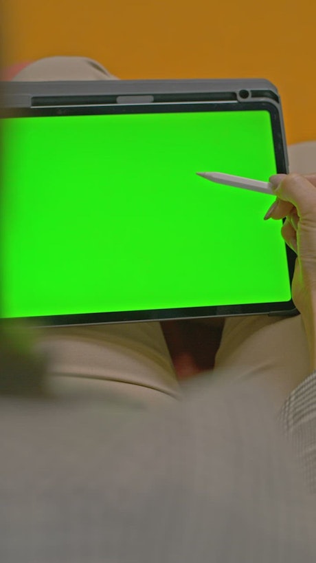 Woman using a stylus on a tablet with a green screen.