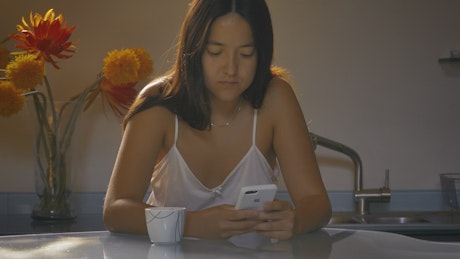 Woman using her cell phone while drinking morning coffee.
