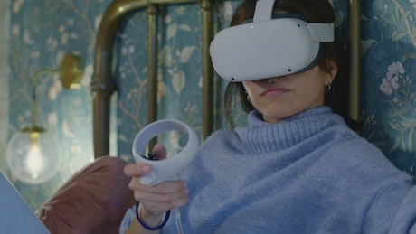 Woman using virtual reality goggles lying on bed.