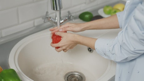 Woman washes red pepper in kitchen sink