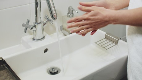Woman washing hands in bathroom sink.