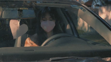 Woman wearing a face mask parking her car.