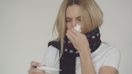 Woman wearing a scarf blowing her nose and checker her temperature.
