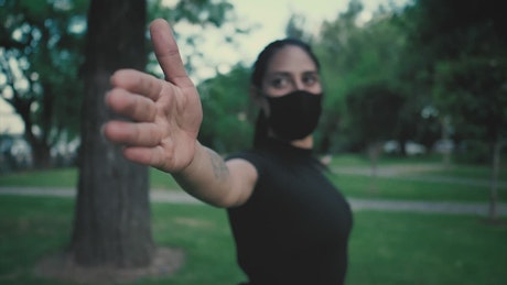 Woman with face mask stretching with her arms in a park