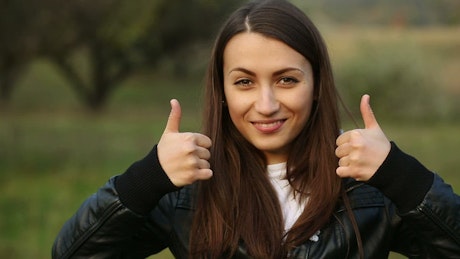 Woman with thumbs up in nature, portrait.