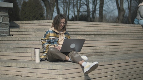 Woman working on her laptop outside in the sun.
