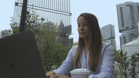 Woman works outdoors on laptop.