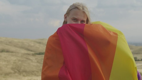 Woman wrapped in the LGBTQIA+ flag blowing in the wind.