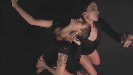 Women dancing together on a dark background.