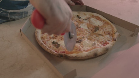 Worker of a pizzeria cutting a pizza