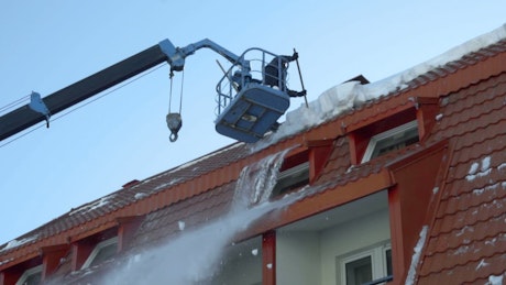 Worker removing snow on the roof of the building
