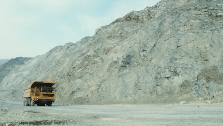Yellow dump truck driving through a barren mining quarry.