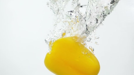 Yellow pepper falling through the water.