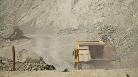 Yellow truck driving along a dusty road in a mining site.
