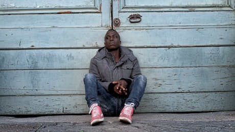 Young black man sits on the footpath bored of waiting.