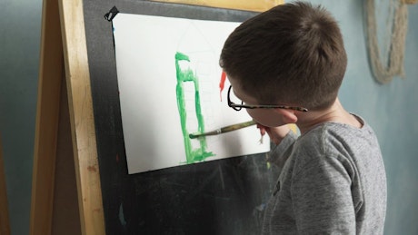 Young boy painting a picture on an easel.