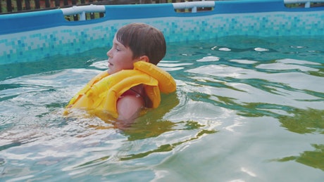 Young boy with inflatable vest swimming in the pool