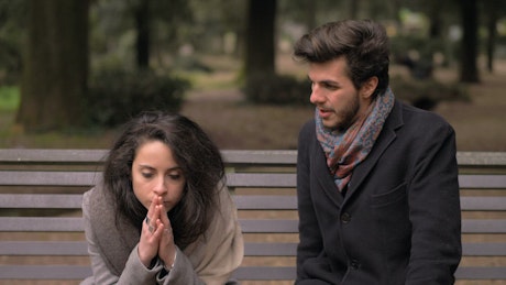 Young couple arguing on a bench outdoors.