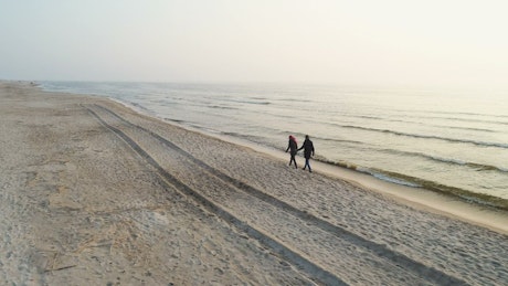 Young couple holding hands walking on beach at sunset.