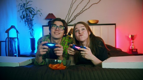 Young couple playing video games on the bed.
