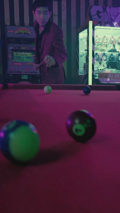 Young gangster playing billiards in a dark arcade