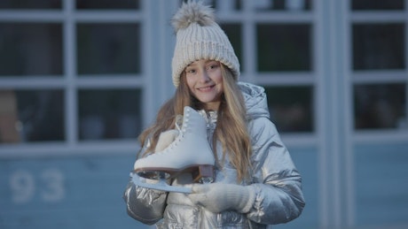 Young girl holding up her ice skating shoes happily.