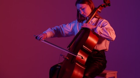 Young girl playing the cello against a purple background.