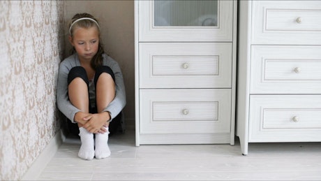 Young girl sitting in a corner of a room crying.