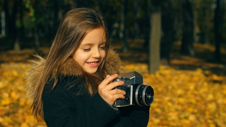 Young girl with a camera standing in a field taking a picture.