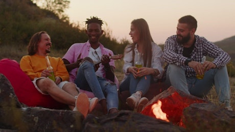 Young group of friend relaxing and laughing around a campfire.