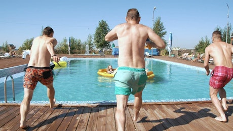Young guys jump into pool splashing girls on float
