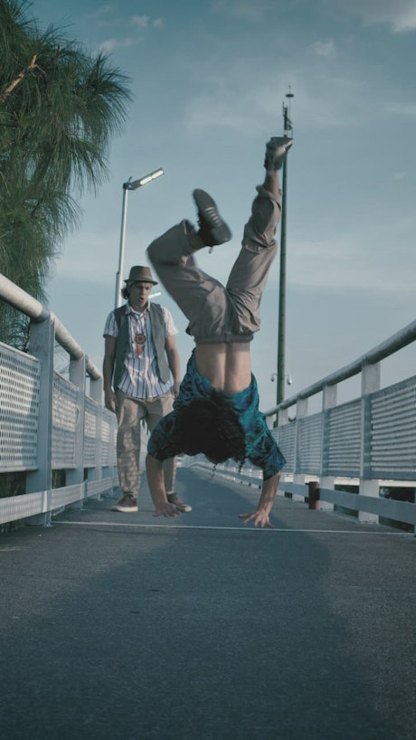 Young man dancing upside down on a pedestrian bridge.