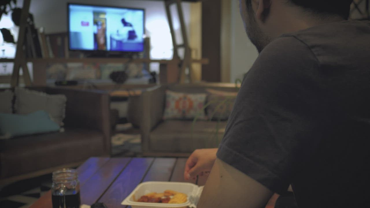 Greedy man watching TV while eating junk, Stock Video