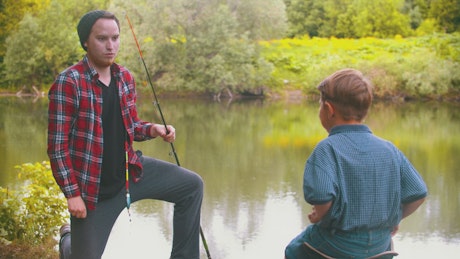 Young man gives a fishing rod to a boy in a lake.