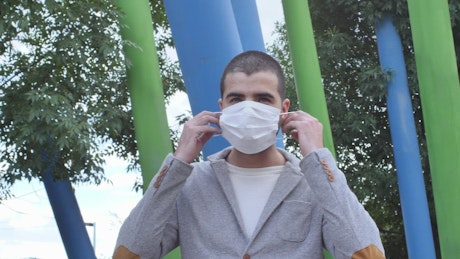 Young man in a park putting on a face mask.