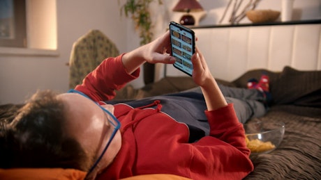 Young man lying on bed scrolling on his cell phone.