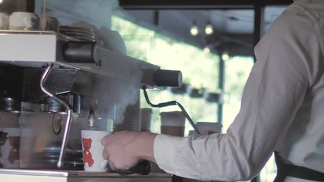 Young man serving hot coffee into a cup