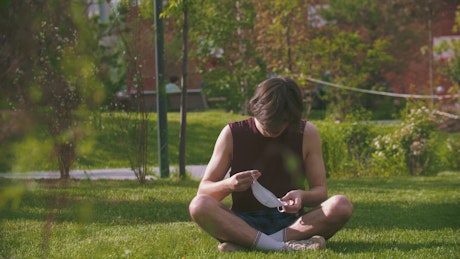 Young man sitting in the park puts on a face mask