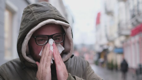Young man with flu blows his nose in the street.