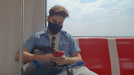 Young man with mask traveling by subway with his cellphone.